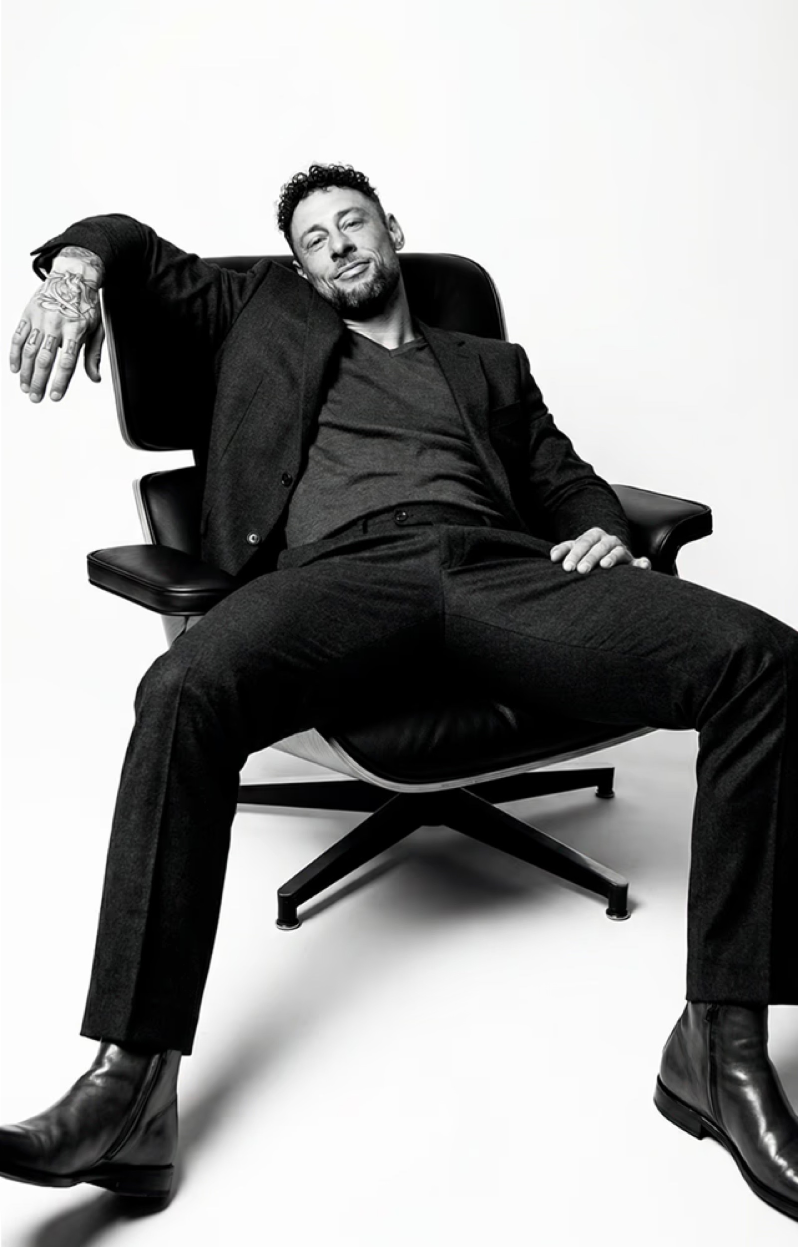 Troy seated in an Eames lounge chair, suit, editorial B&W